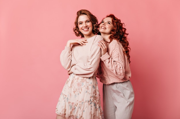 Ragazze allegre che esprimono felicità su sfondo rosa. Vista frontale di due signore ben vestite sorridendo alla telecamera.