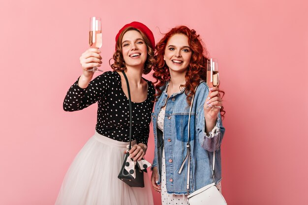 Ragazze beate che sollevano bicchieri di vino. Vista frontale di amici che celebrano qualcosa con champagne.