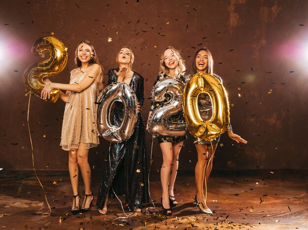 Ragazze bellissime felici in eleganti abiti da festa sexy con palloncini oro e argento 2020