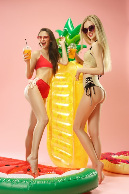 Ragazze carine in costume da bagno che propone allo studio. Adolescenti caucasici del ritratto di estate su uno sfondo rosa.