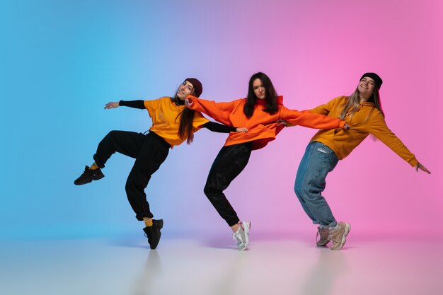 Ragazze che ballano hip-hop in abiti eleganti su sfondo sfumato studio alla luce al neon.