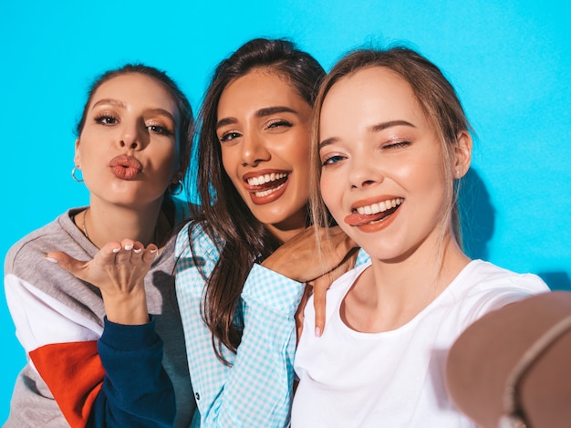 Ragazze che prendono le foto dell'autoritratto del selfie sullo smartphone Modelli che posano vicino alla parete blu in studio.