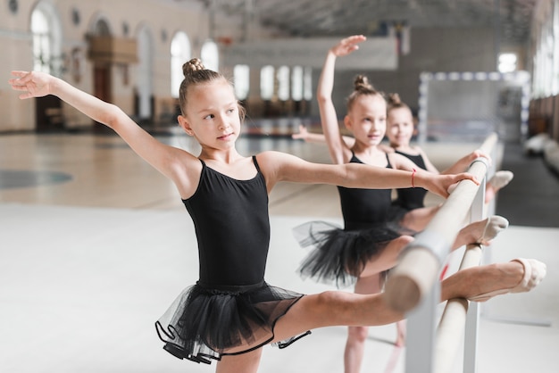 Ragazze della ballerina in tutu nero che allunga le loro gambe sulla barra