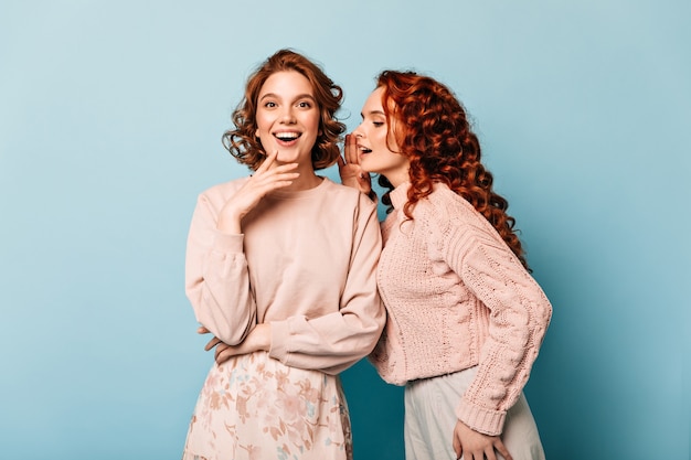 Ragazze di buon umore parlando su sfondo blu. Studio shot di allegri amici.