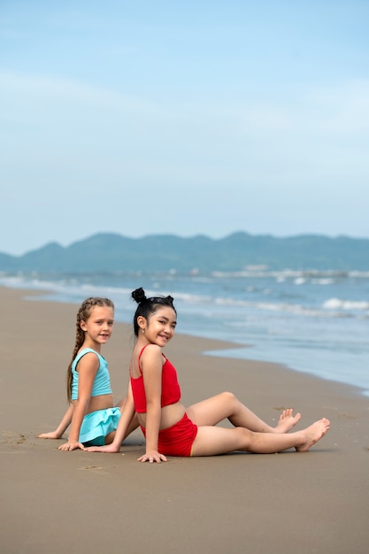 Ragazze di smiley di vista laterale che si siedono sulla spiaggia