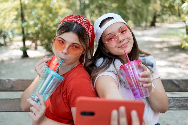 Ragazze di tiro medio che prendono selfie con bevande