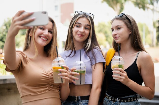 Ragazze di tiro medio con bevande che prendono selfie