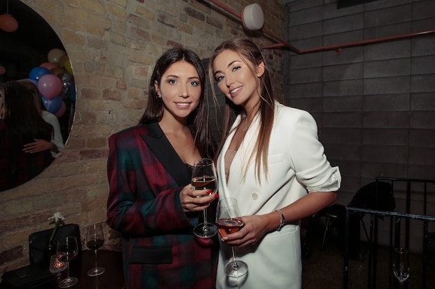 Ragazze fantasiose che si divertono a una festa. Bionda che indossa giacca bianca e accessori, trucco naturale sul viso e capelli alla moda. Donna castana in un vestito alla moda nero