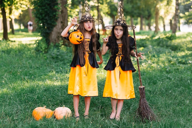 Ragazze in costumi strega facendo facce tenendo la scopa e la zucca