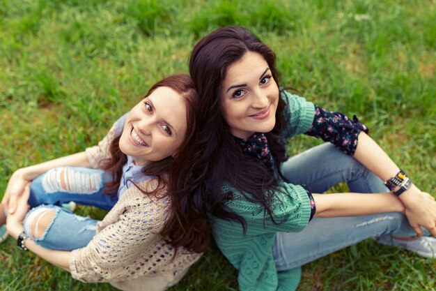 Ragazze sorridenti che si siedono schiena contro schiena sull'erba