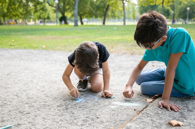 Ragazzi concentrati seduti e disegnando con gessetti colorati. Concetto di infanzia e creatività