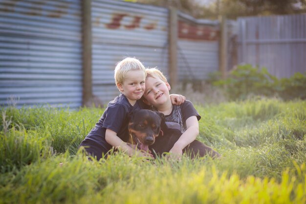 Ragazzini carini seduti allegramente sull'erba e in posa con un cane rottweiler