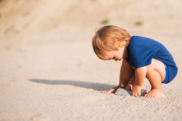 Ragazzino alla spiaggia che gioca con la sabbia