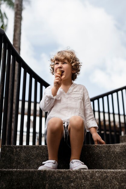 Ragazzino del colpo pieno che mangia il cono gelato