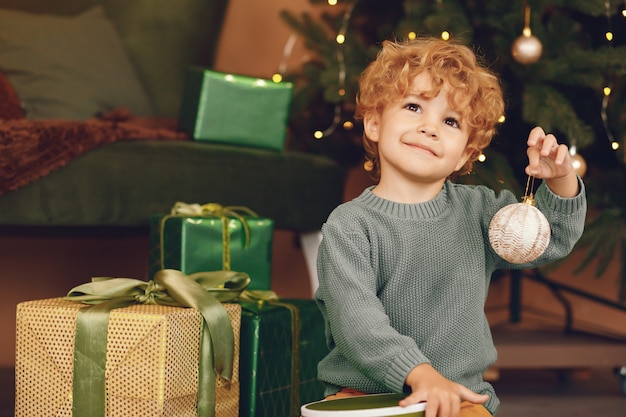 Ragazzino vicino all'albero di Natale in un maglione grigio