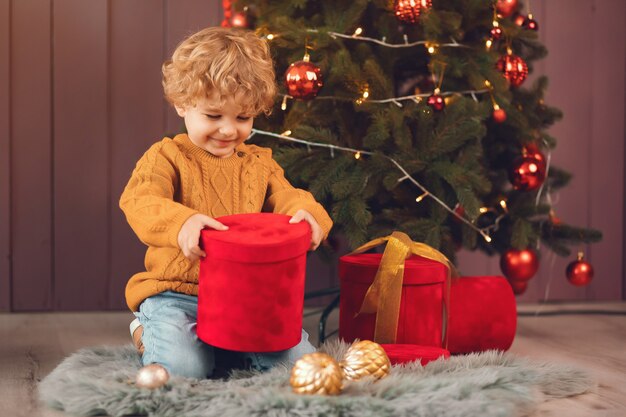 Ragazzino vicino all'albero di Natale in un maglione marrone