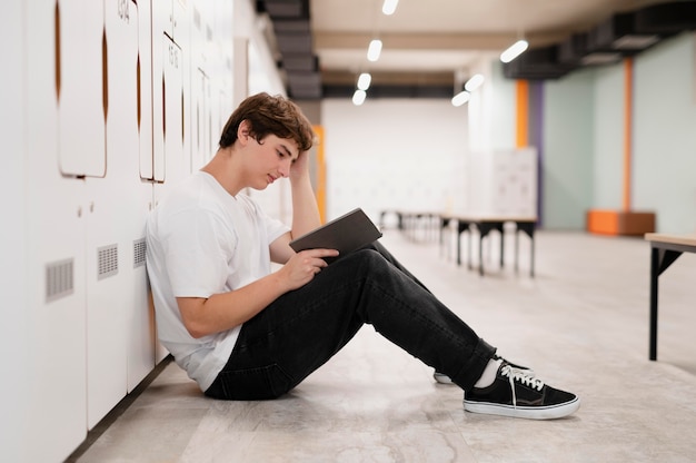 Ragazzo a tutto campo che legge sul pavimento a scuola