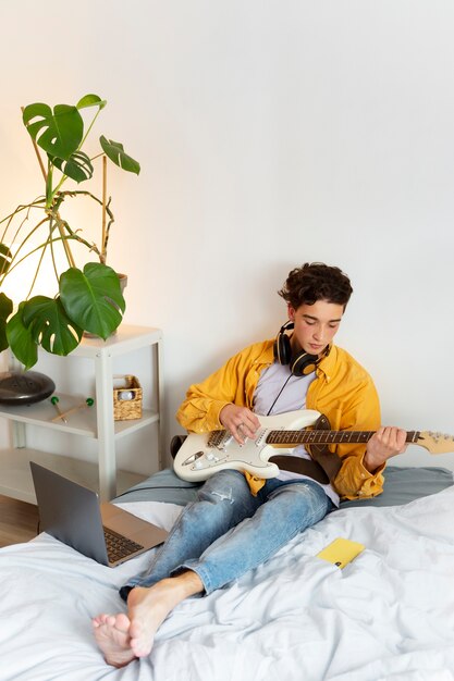Ragazzo a tutto campo che suona la chitarra a casa