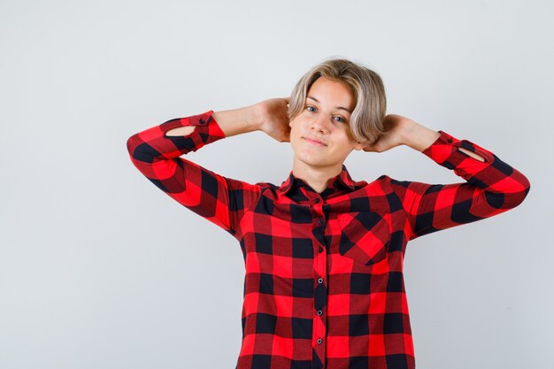 Ragazzo abbastanza teenager con le mani dietro la testa in camicia a quadri e guardando rilassato. vista frontale.