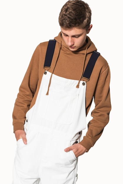 Ragazzo adolescente in salopette bianca e felpa con cappuccio marrone streetwear servizio fotografico
