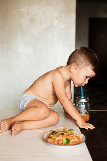 Ragazzo adorabile che beve il succo e che mangia pasta