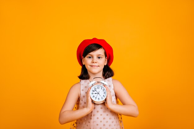 Ragazzo adorabile che tiene grande orologio. bambino caucasico entusiasta isolato sulla parete gialla.