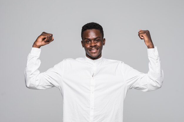 Ragazzo africano bello allegro in breve camicia bianca che fa sì gesto mentre eccitato per la vittoria. Estatico giovane tifo che tifa ed esprime sostegno.