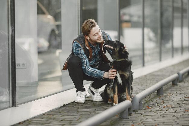 Ragazzo alla moda che gioca con un cane. Uomo in città d'autunno.