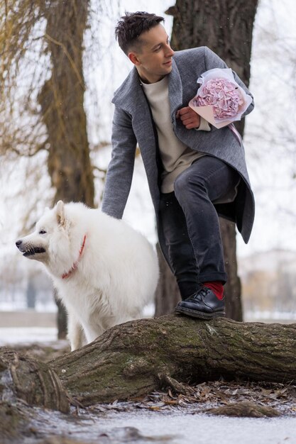Ragazzo amico con un mazzo di fiori rosa ortensia che aspetta la sua ragazza e cammina e gioca con un cane. all'aperto mentre cade la neve. Concetto di San Valentino, proposta di matrimonio. l'uomo va