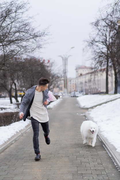 Ragazzo amico con un mazzo di fiori rosa ortensia che aspetta la sua ragazza e cammina e gioca con un cane. all'aperto mentre cade la neve. Concetto di San Valentino, proposta di matrimonio. l'uomo va