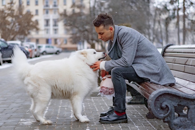 Ragazzo amico con un mazzo di fiori rosa ortensia che aspetta la sua ragazza e cammina e gioca con un cane. all'aperto mentre cade la neve. Concetto di San Valentino, proposta di matrimonio. l'uomo va