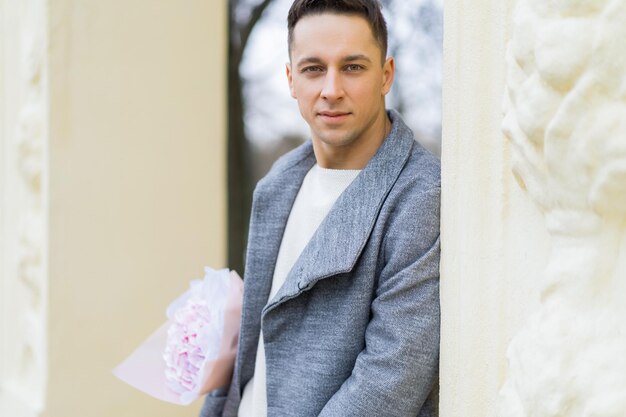 Ragazzo amico con un mazzo di fiori rosa ortensia in attesa della sua ragazza all'aperto mentre la neve sta cadendo. Concetto di San Valentino, proposta di matrimonio. l'uomo va ad un appuntamento.