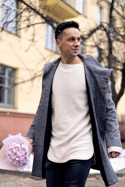 Ragazzo amico con un mazzo di fiori rosa ortensia in attesa della sua ragazza all'aperto mentre la neve sta cadendo. Concetto di San Valentino, proposta di matrimonio. l'uomo va ad un appuntamento.