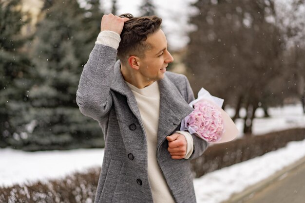 Ragazzo amico con un mazzo di fiori rosa ortensia in attesa della sua ragazza all'aperto mentre la neve sta cadendo. Concetto di San Valentino, proposta di matrimonio. l'uomo va ad un appuntamento.