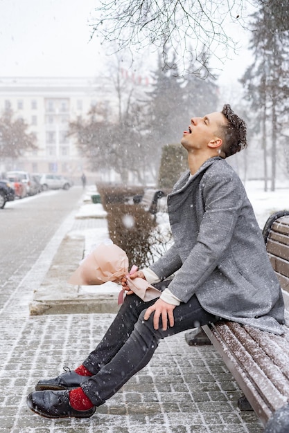 Ragazzo amico con un mazzo di fiori rosa ortensia in attesa della sua ragazza all'aperto mentre la neve sta cadendo. Concetto di San Valentino, proposta di matrimonio. l'uomo va ad un appuntamento.