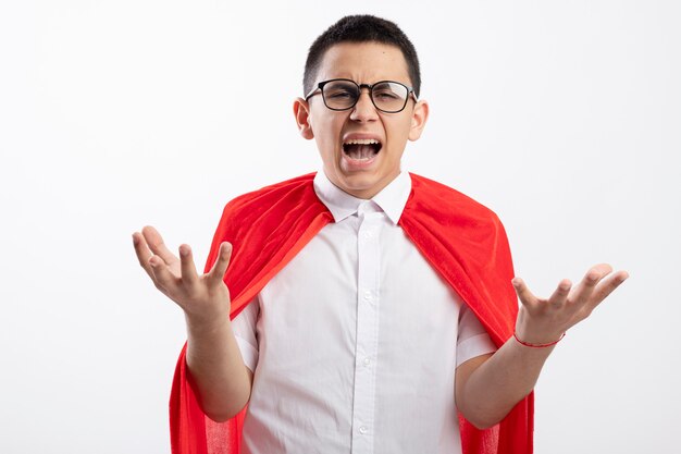 Ragazzo arrabbiato giovane supereroe in mantello rosso con gli occhiali che guarda l'obbiettivo che mostra le mani vuote isolate su priorità bassa bianca