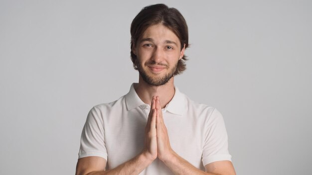 Ragazzo attraente tenendo i palmi premuti insieme per chiedere qualcosa guardando la fotocamera isolata su sfondo grigio Giovane che chiede favore