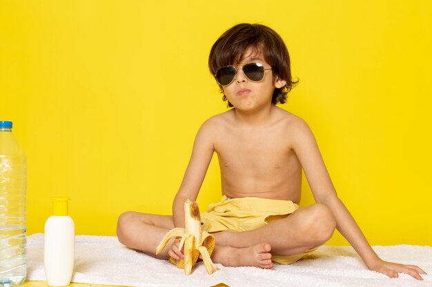 ragazzo bambino vista frontale in occhiali da sole sulla scrivania gialla