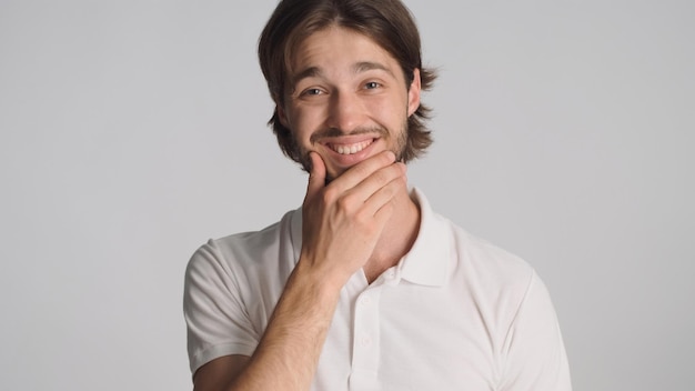 Ragazzo barbuto attraente che sorride alla macchina fotografica su sfondo bianco Uomo bruna positivo che sembra felice