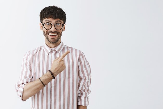 Ragazzo barbuto elegante divertito in posa contro il muro bianco con gli occhiali