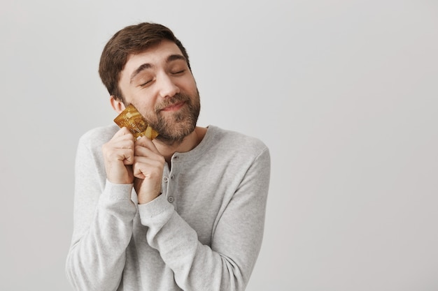 Ragazzo barbuto felice felice che abbraccia la carta di credito fredda