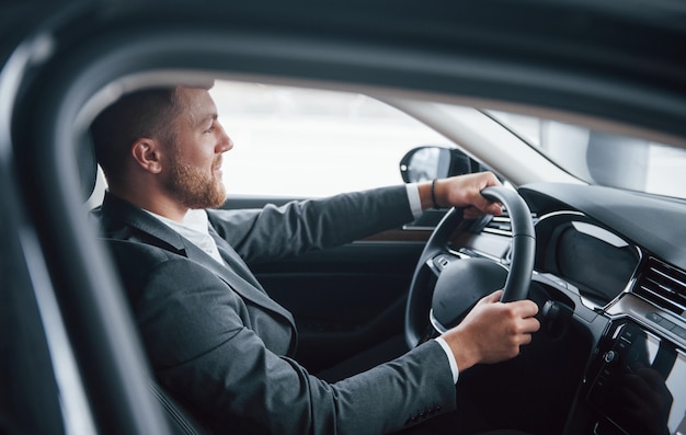 Ragazzo barbuto felice. Uomo d'affari moderno che prova la sua nuova automobile nel salone dell'automobile