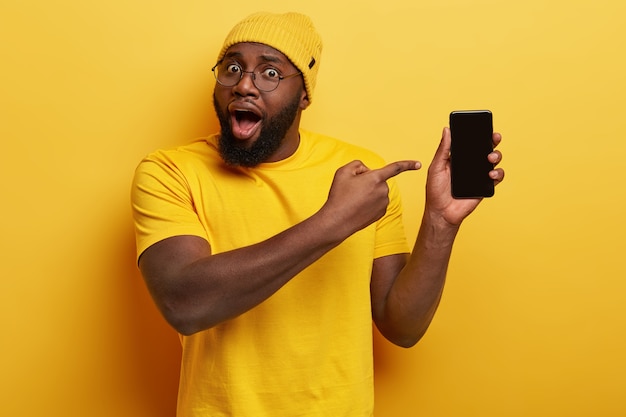 Ragazzo bello stupito con gli occhiali in posa con il suo telefono