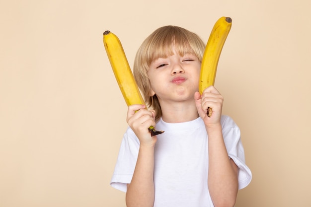 ragazzo biondo con le banane in maglietta bianca sulla parete rosa