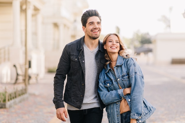 Ragazzo brunetta che cammina con la ragazza nel fine settimana. Ritratto all'aperto di giovani felici che godono della data.