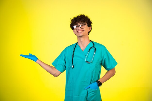 Ragazzo capelli ricci in uniforme medica e maschere per le mani che mostrano qualcosa.