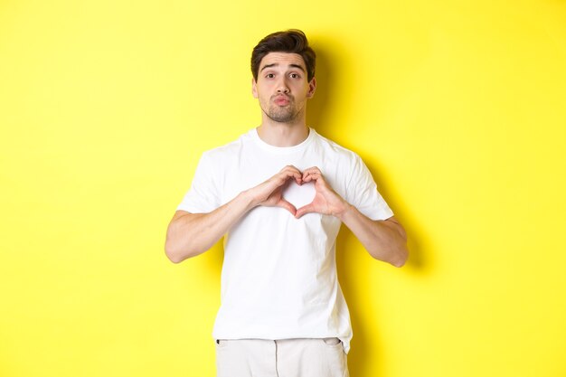 Ragazzo carino arriccia le labbra e aspetta un bacio, mostrando il gesto del cuore. Concetto di amore e romanticismo