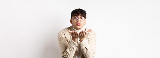 Ragazzo carino che manda un bacio d'aria alla telecamera il giorno di san valentino felice che sembra tenero all'amante in piedi i