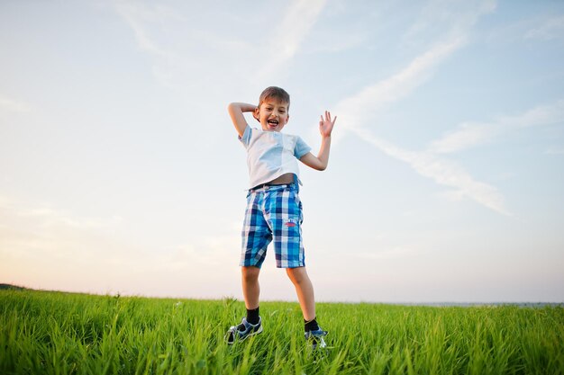 Ragazzo carino che salta nel campo di erba verde alla sera