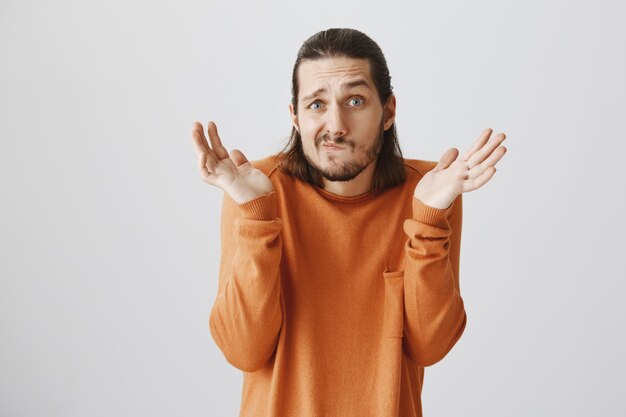 Ragazzo carino confuso e perplesso che scrolla le spalle, alzando le mani senza tracce